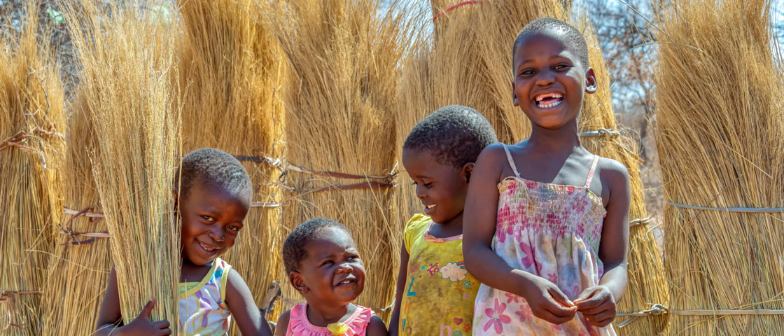Group of smiling African children standing among upright bundles of straw