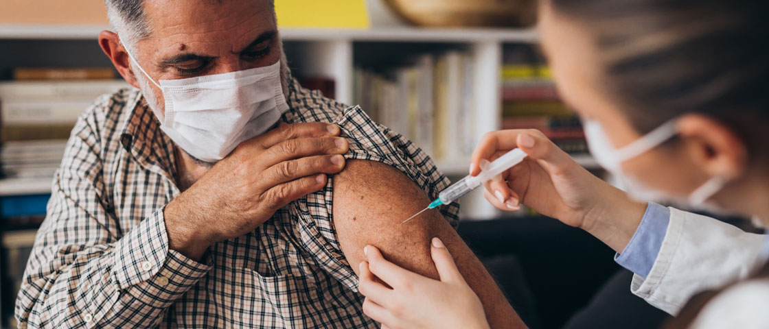 A person wearing a mask receives a shot in their arm