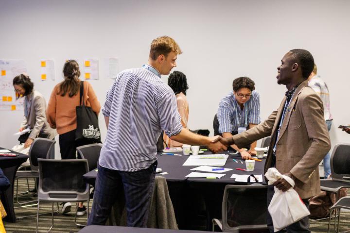Two people shaking hands in a meeting room with other people